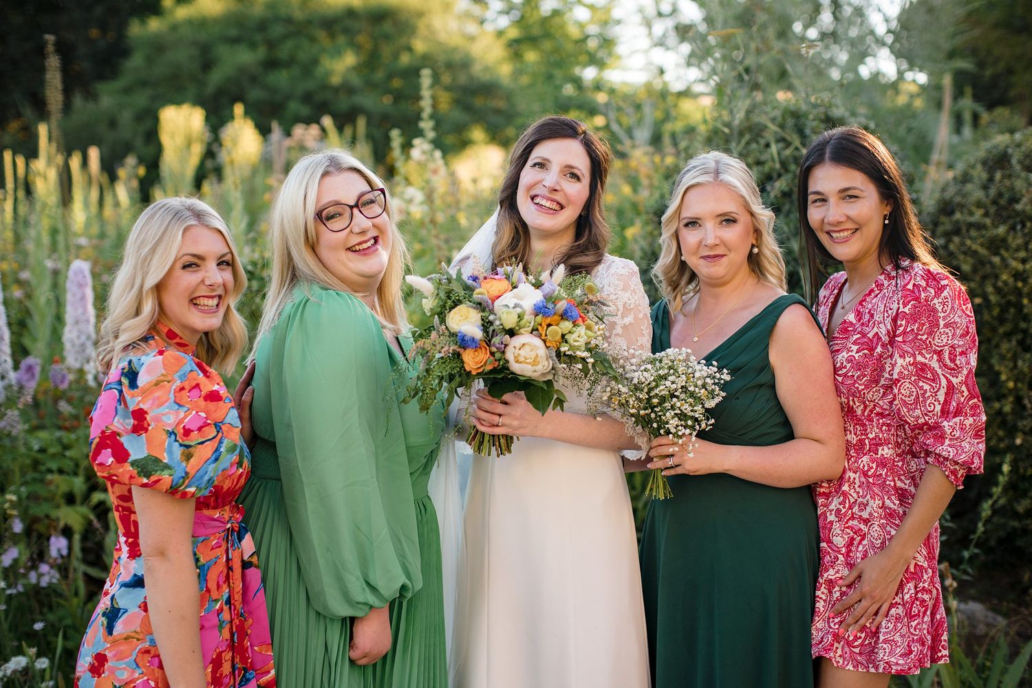 Wedding party wearing colourful dresses posing together in a garden setting at Healy Events wedding venue.