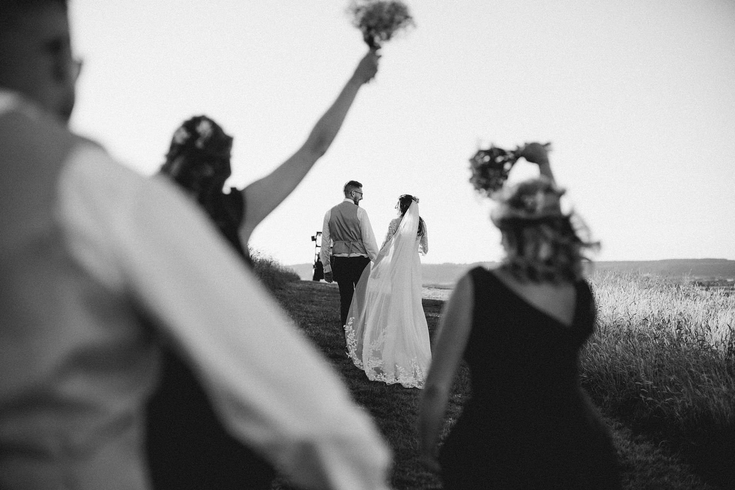 Black and white wedding photo showing bridal party walking up grassy hill with silhouettes in foreground near Kentville at Healy Events
