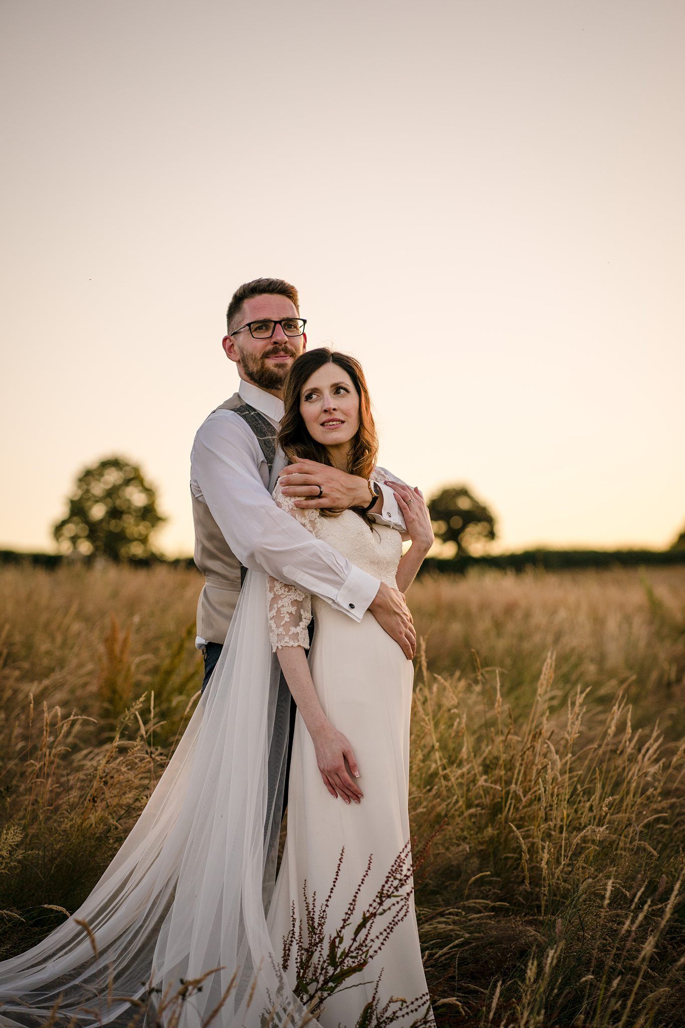 A romantic sunset wedding photo of a couple embracing in a golden field with long grass and warm evening light near Healy Events venue