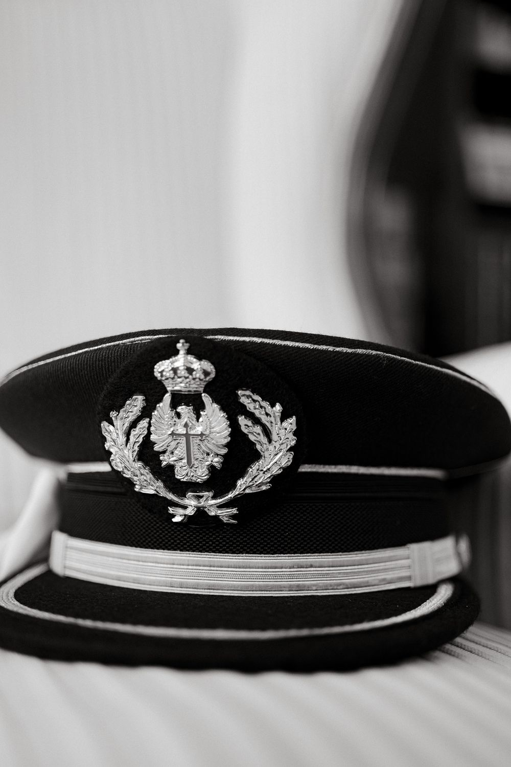 Black military dress cap with ornate silver crown and laurel wreath emblem.