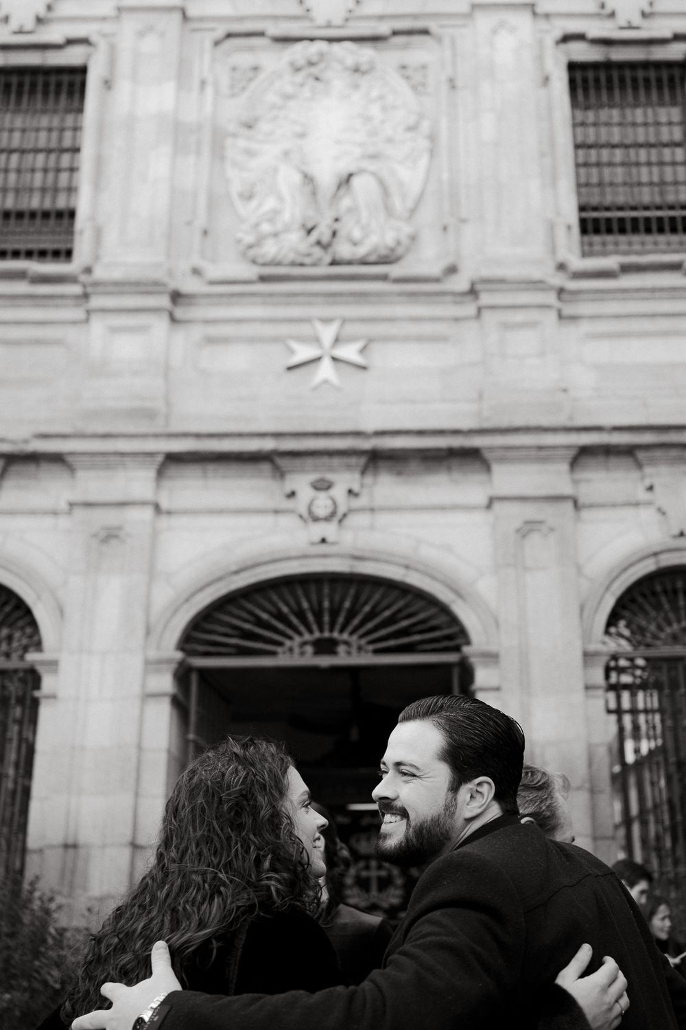 Couple embracing and laughing outside historic building with ornate facade.