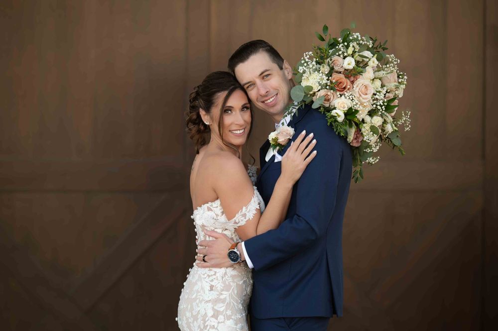 A romantic wedding portrait showing a couple holding a beautiful floral bouquet against a brown backdrop.