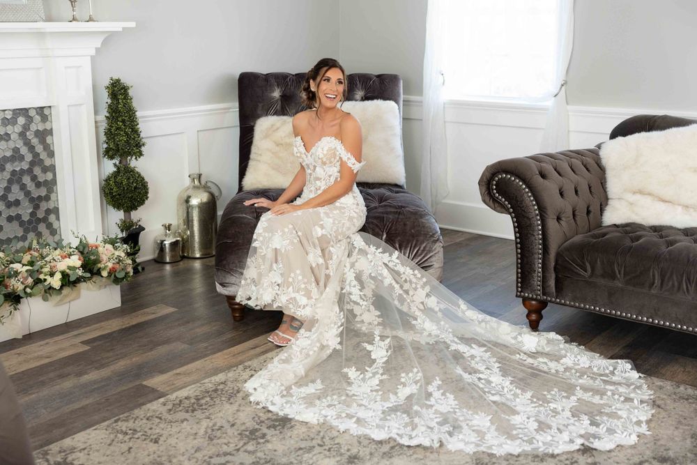 Elegant lace wedding dress with dramatic Cathedral length train flows across dark hardwood floor by leather couch.
