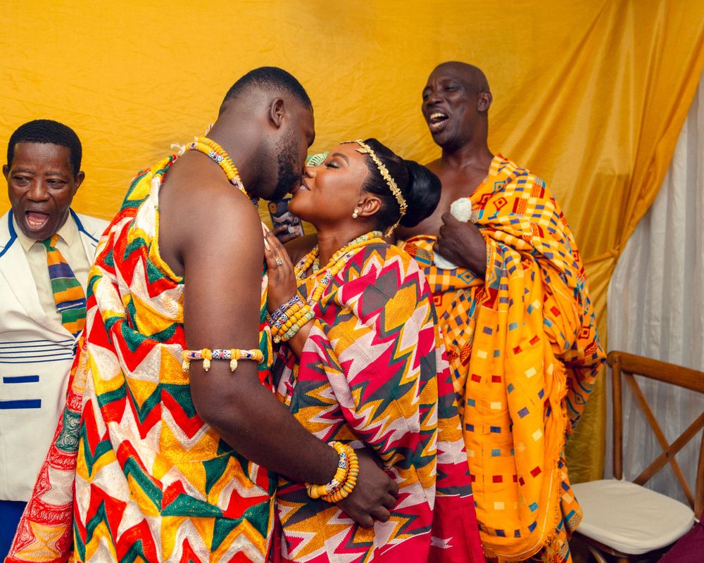 Emotional moment during traditional ceremony with participants in vibrant kente clothing.