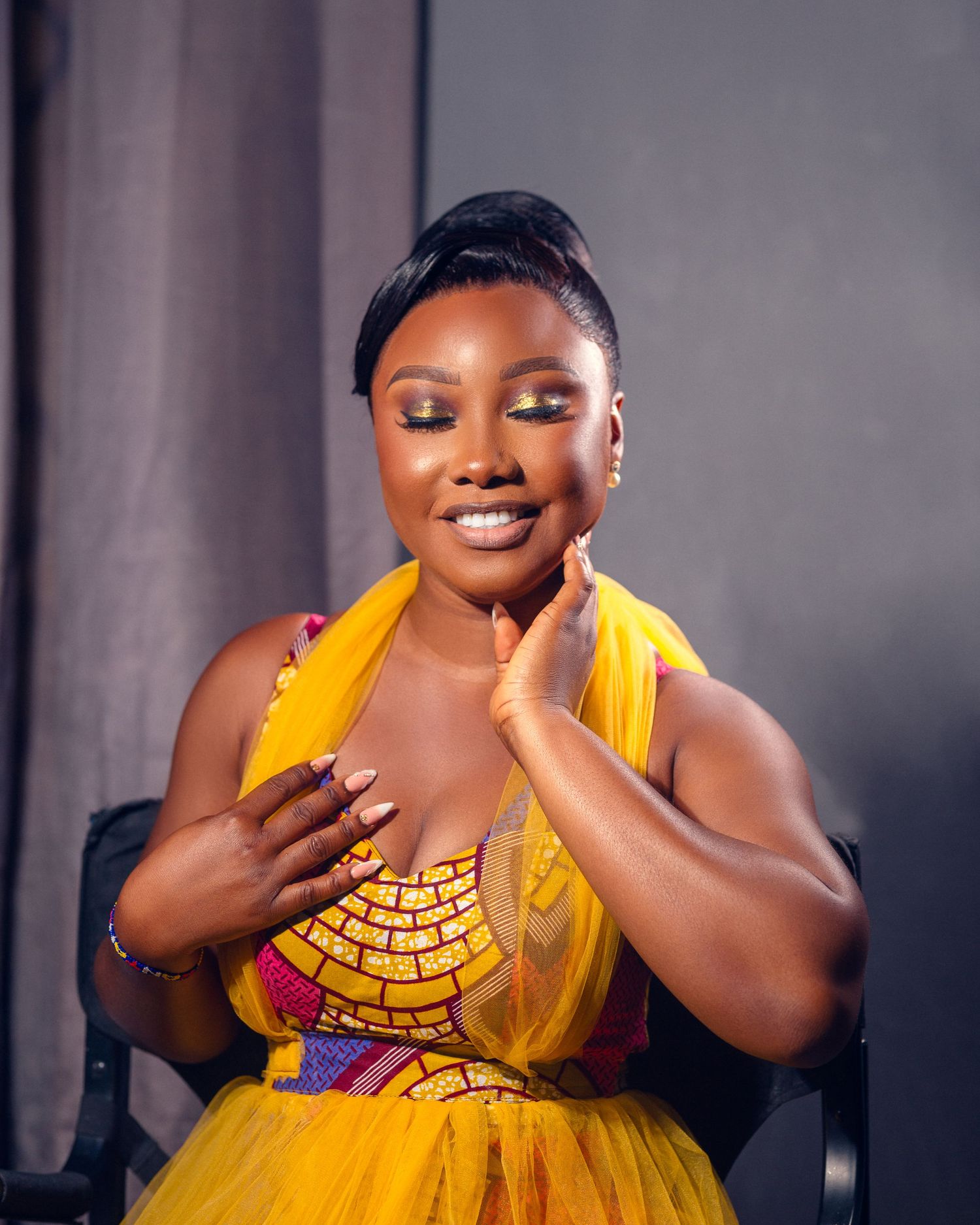 Portrait in bright yellow flowing gown with decorative gold beaded bodice detail against dark studio backdrop.