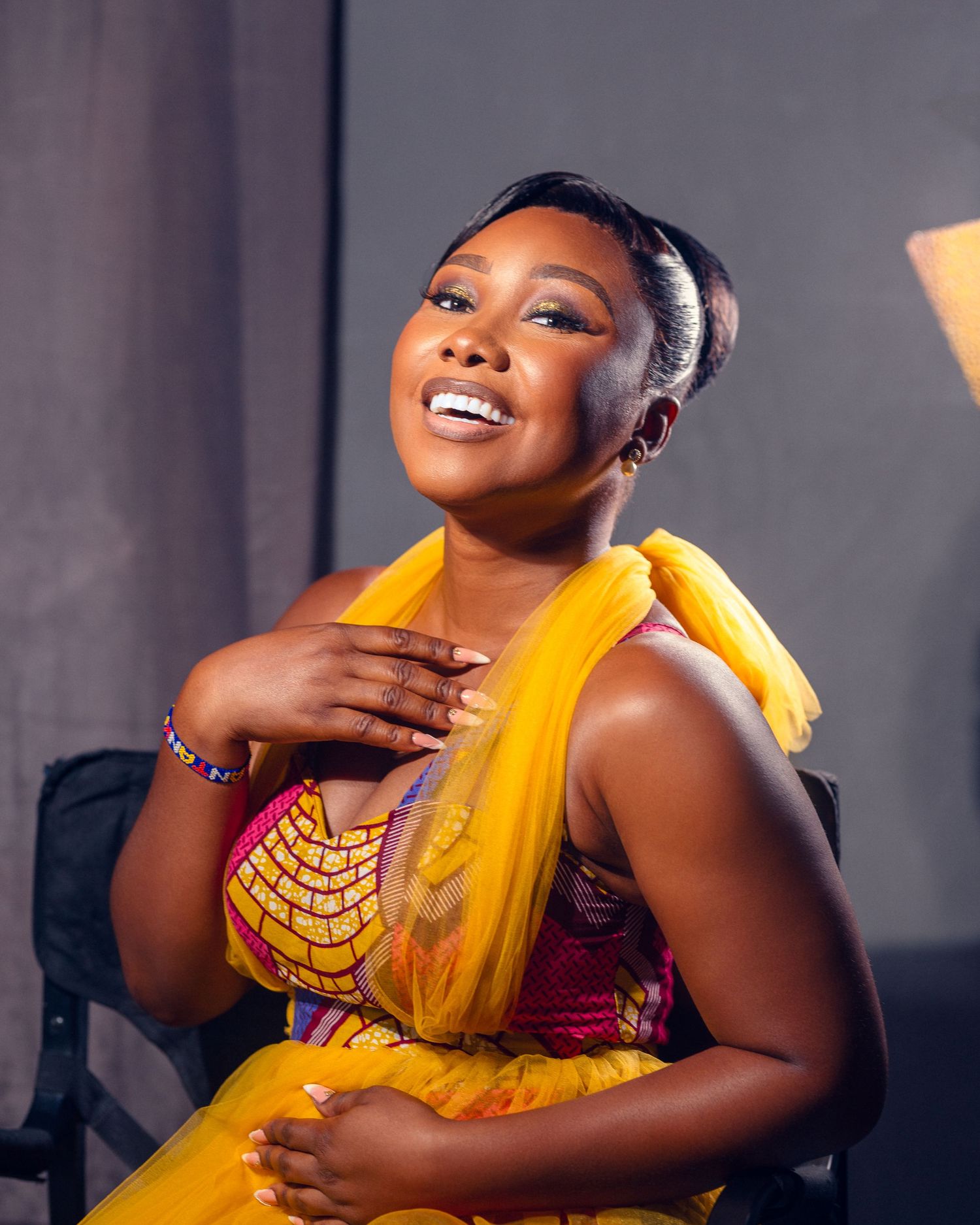Woman in yellow and red traditional attire poses elegantly against dark background.