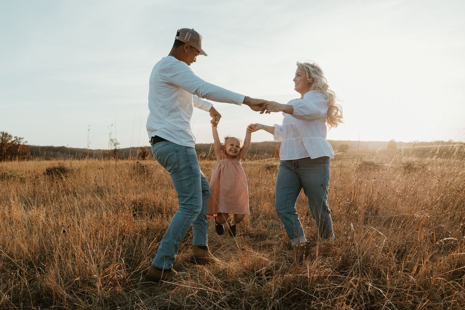 Family dancing together in tall grass field during golden hour sunset.