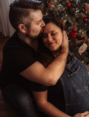 A couple embraces in front of a decorated Christmas tree with red ornaments.