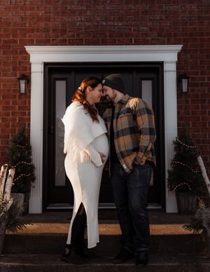 A cozy winter couple in warm clothes shares an intimate moment by a decorated front door.