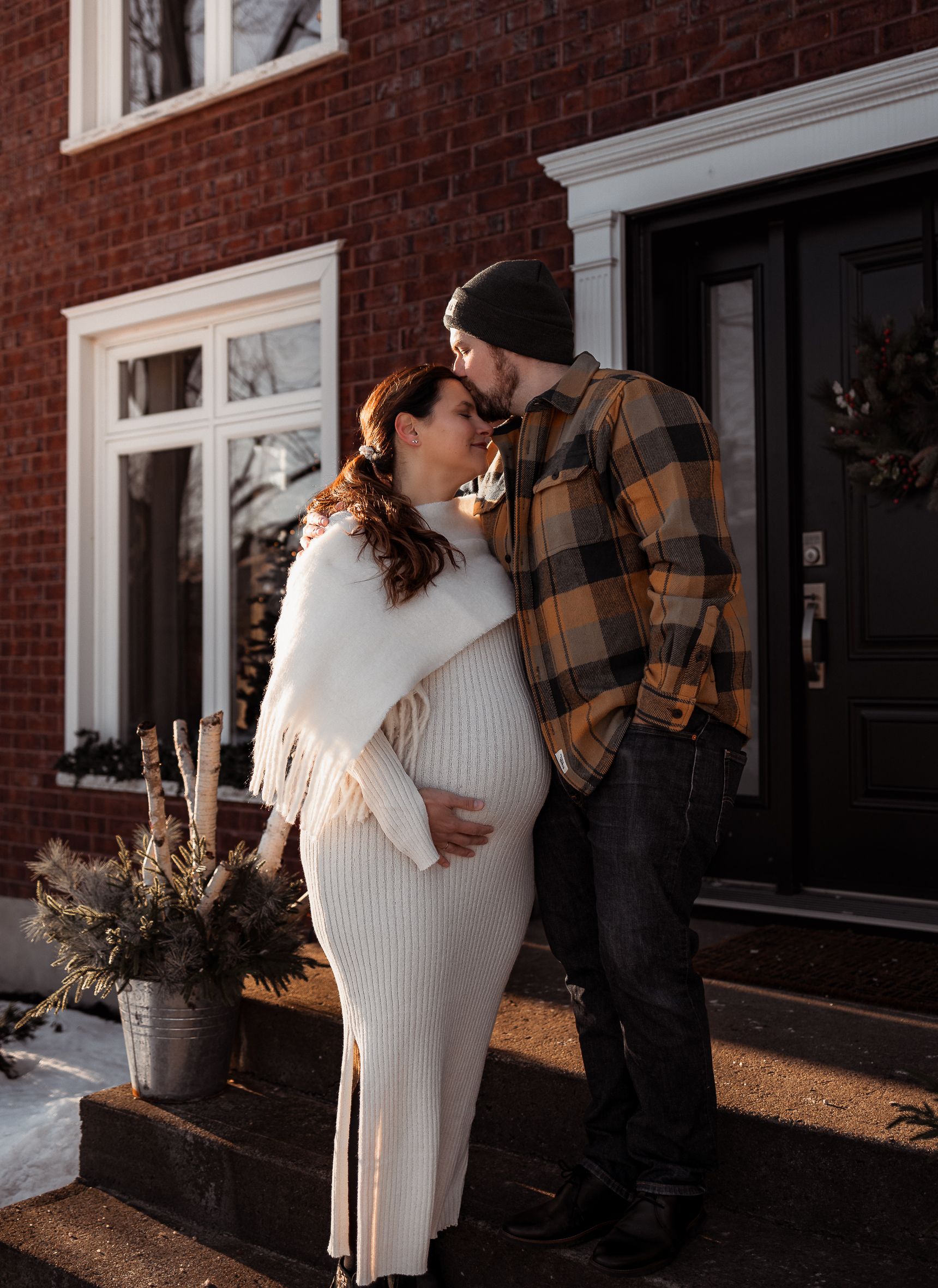 Intimate maternity moment with couple in casual wear against brick building.
