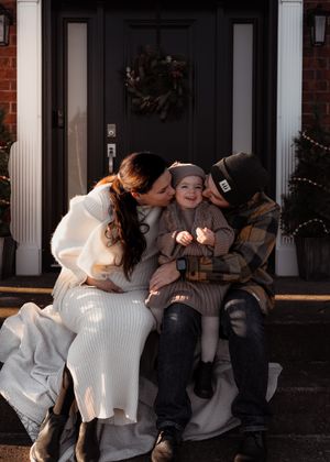 Family sitting on front porch steps of brick house during winter season.