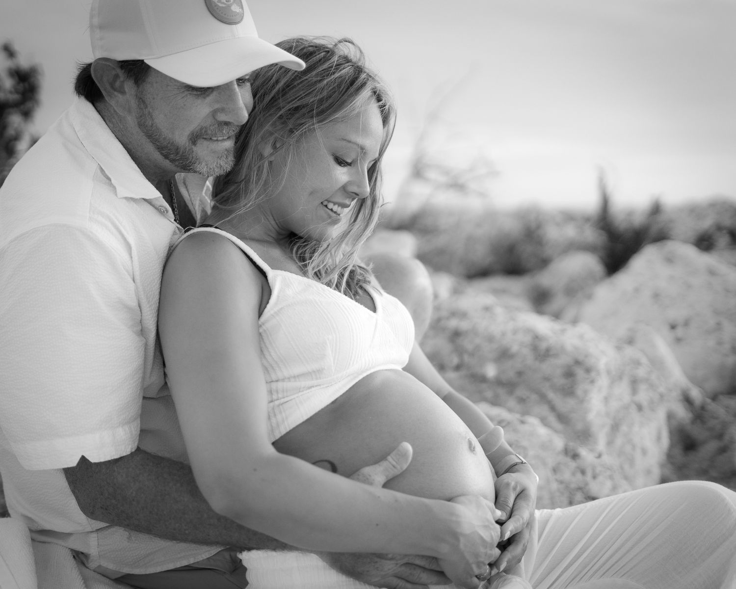 An expectant couple shares an intimate black and white moment outdoors.