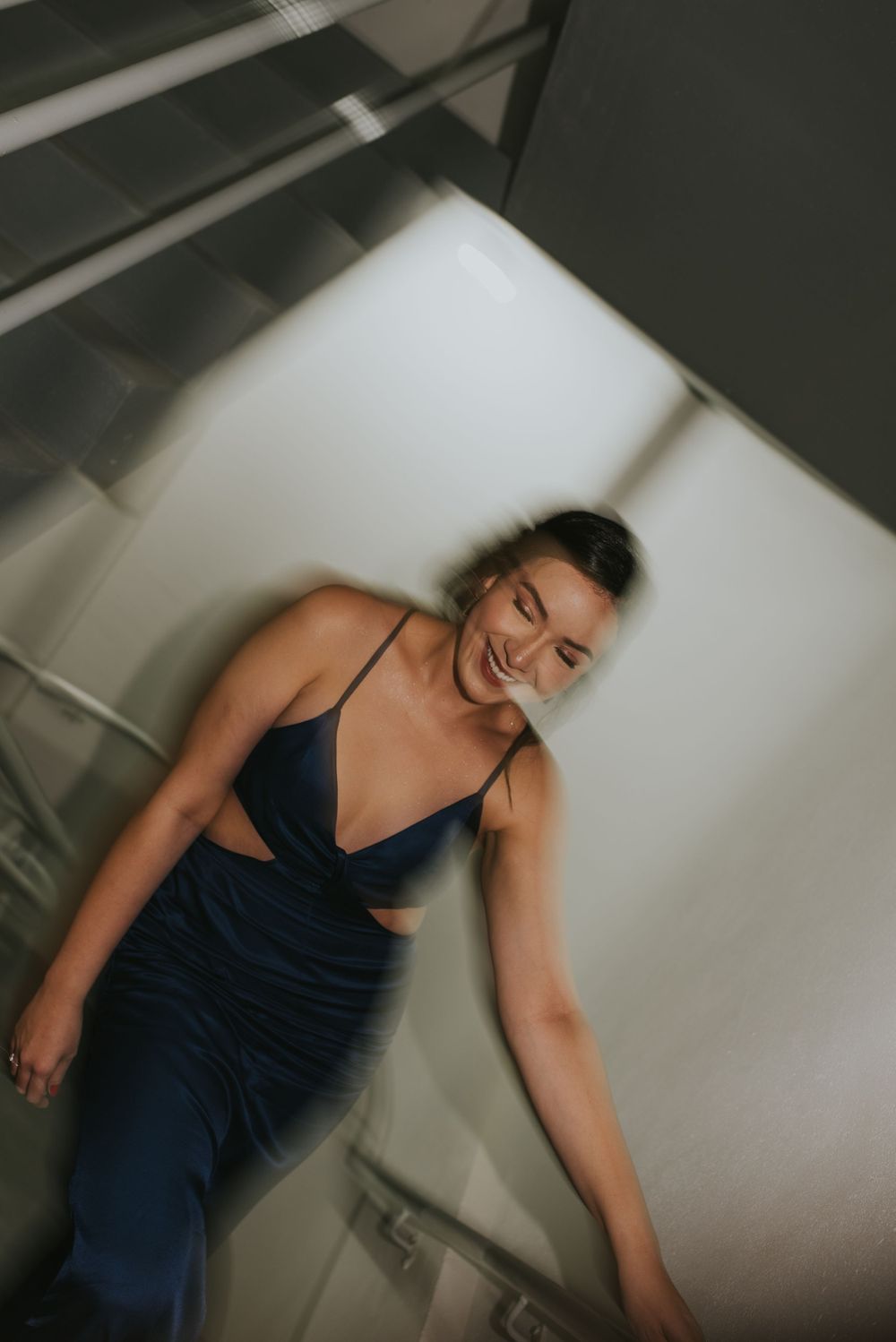 Person in a navy blue dress laughs while posing against a white wall.