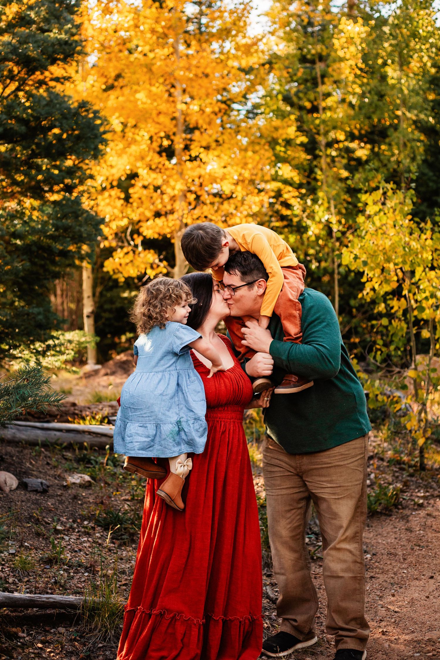 A family cuddles together in autumn woods surrounded by golden yellow foliage at sunset.