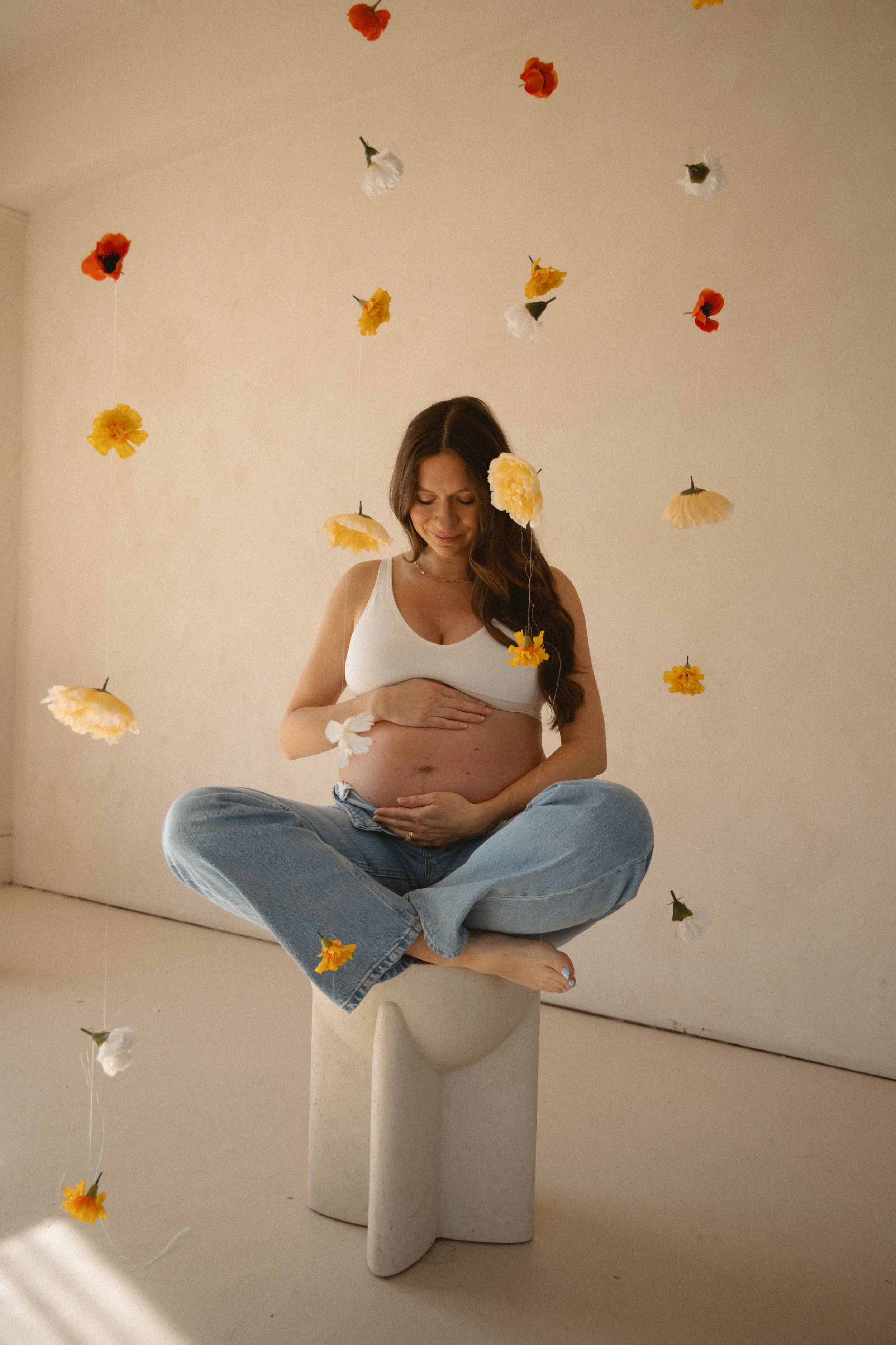 In-studio maternity session during a spring mini session in a studio in Vancouver. Pregnant mom sitting cross-legged in flower curtain.