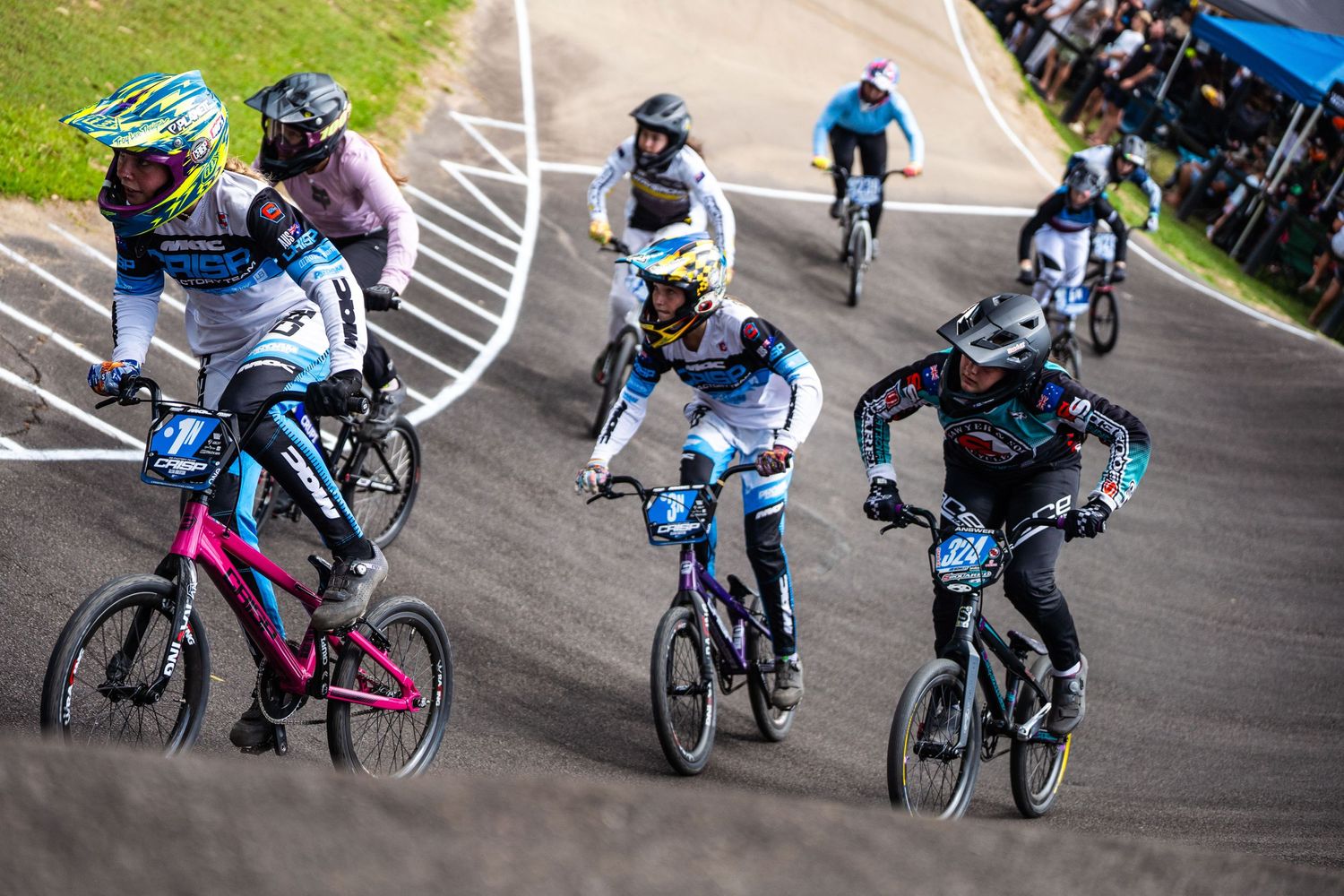 BMX racers navigate a turn on the track during an intense competition with colorful jerseys and protective gear.