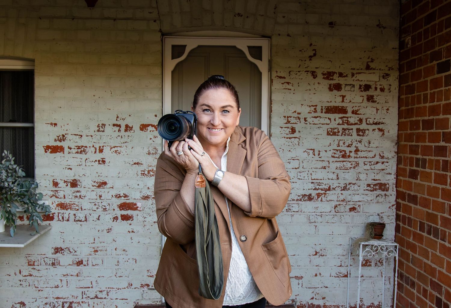 Photographer wearing a white shirt takes picture with professional camera against rustic brick wall background.