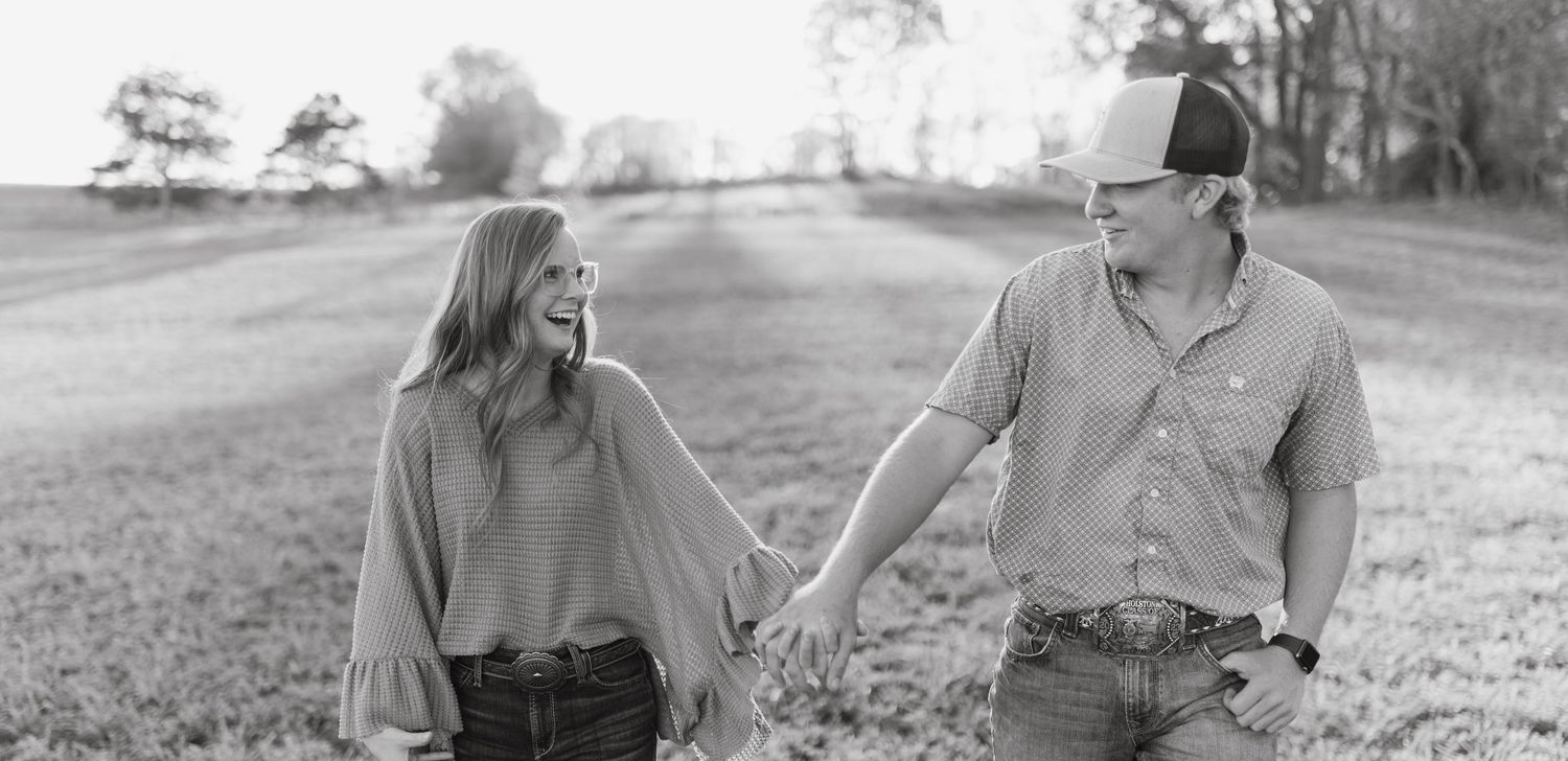 Black and white photo of a couple walking and holding hands in a scenic field.