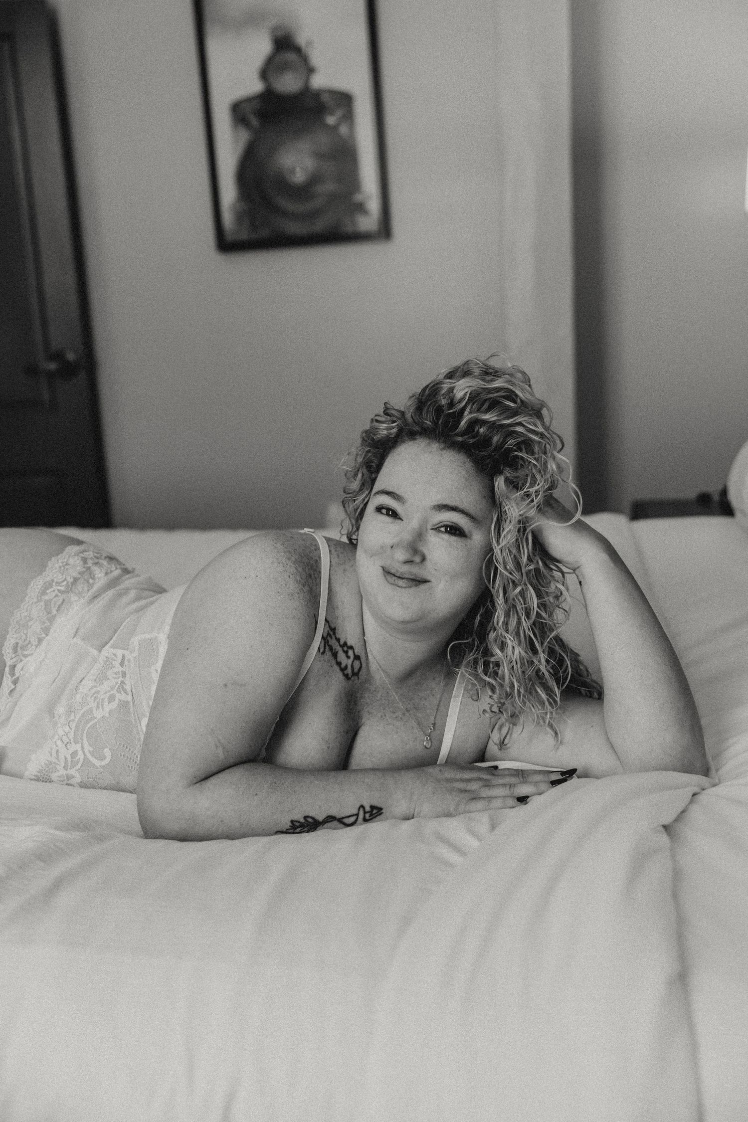 Artistic black and white boudoir portrait on white bedding showing soft natural lighting.