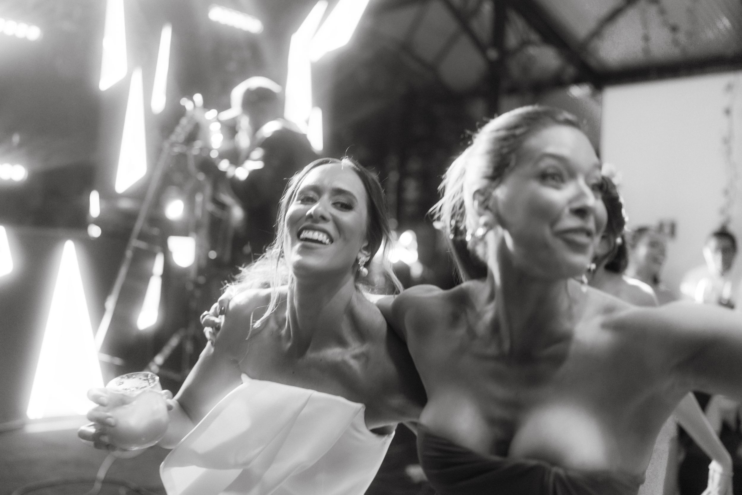Two women dancing and laughing at a celebration in black and white film style.