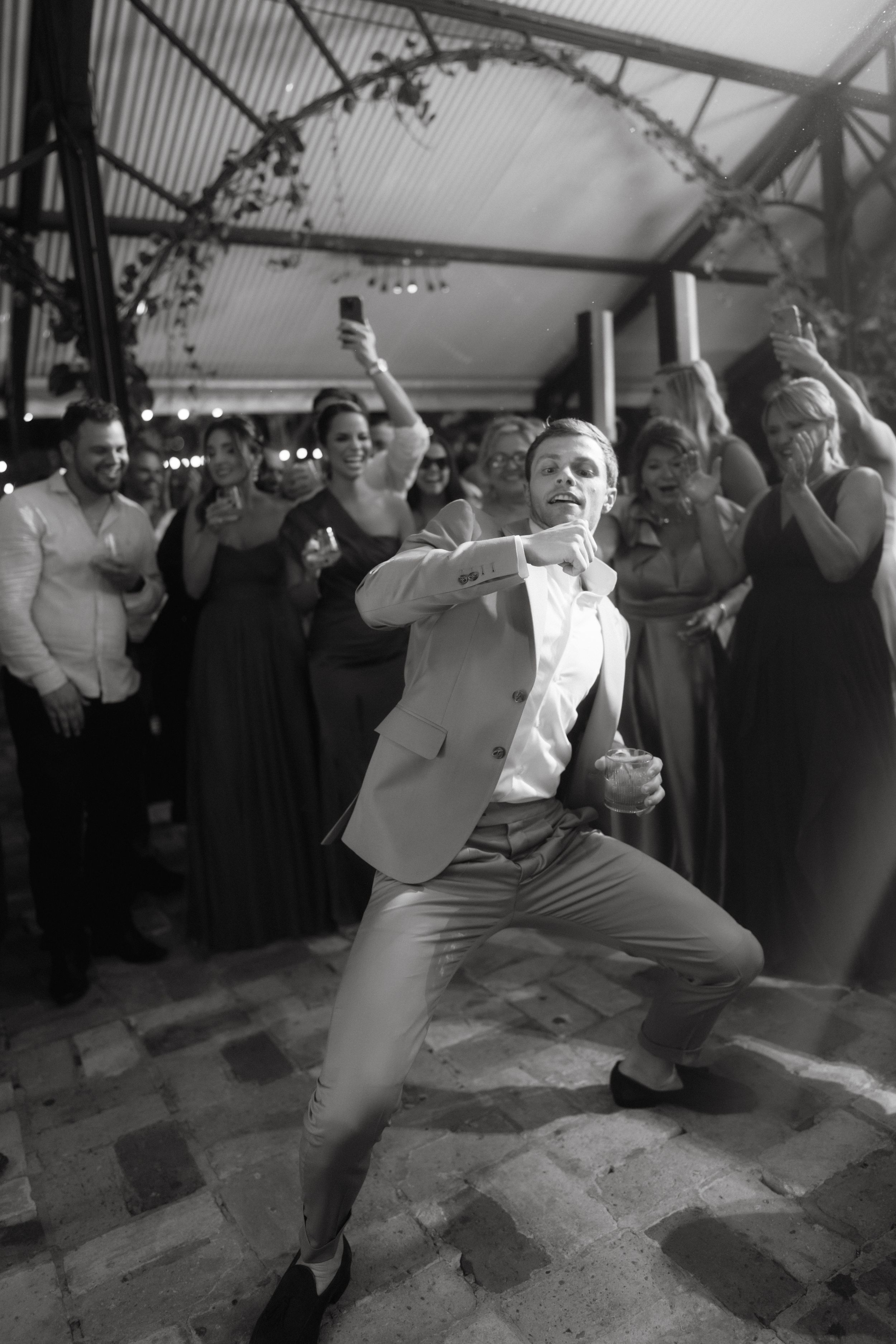 Man in light suit performing energetic dance moves at wedding reception.