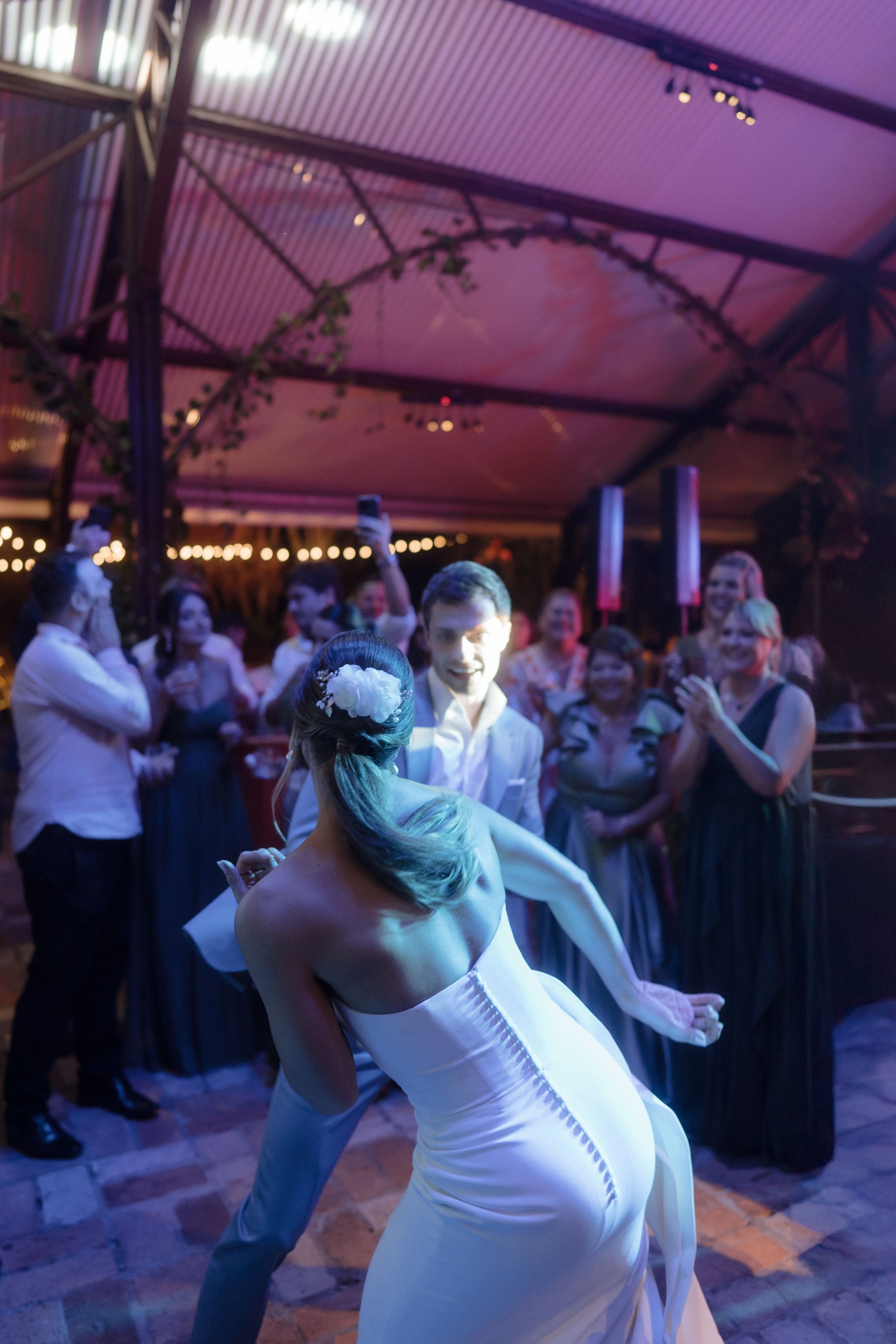 Wedding couple performing first dance under purple lighting with guests watching.