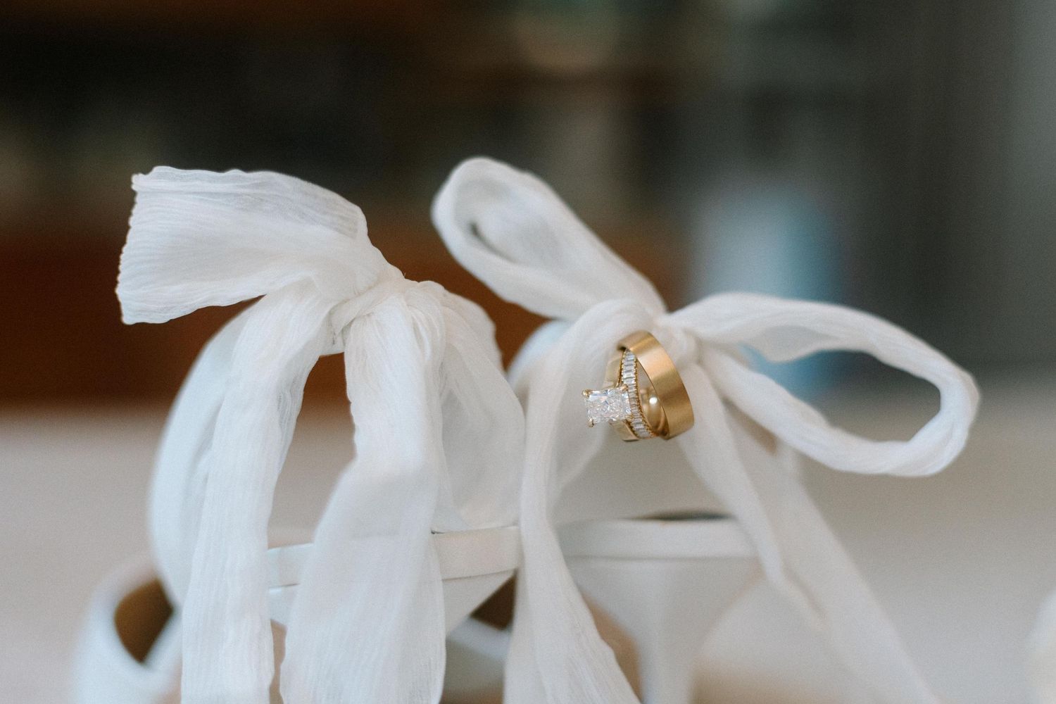 Wedding rings sparkle against delicate white satin ribbons tied in bows during a bridal preparation.