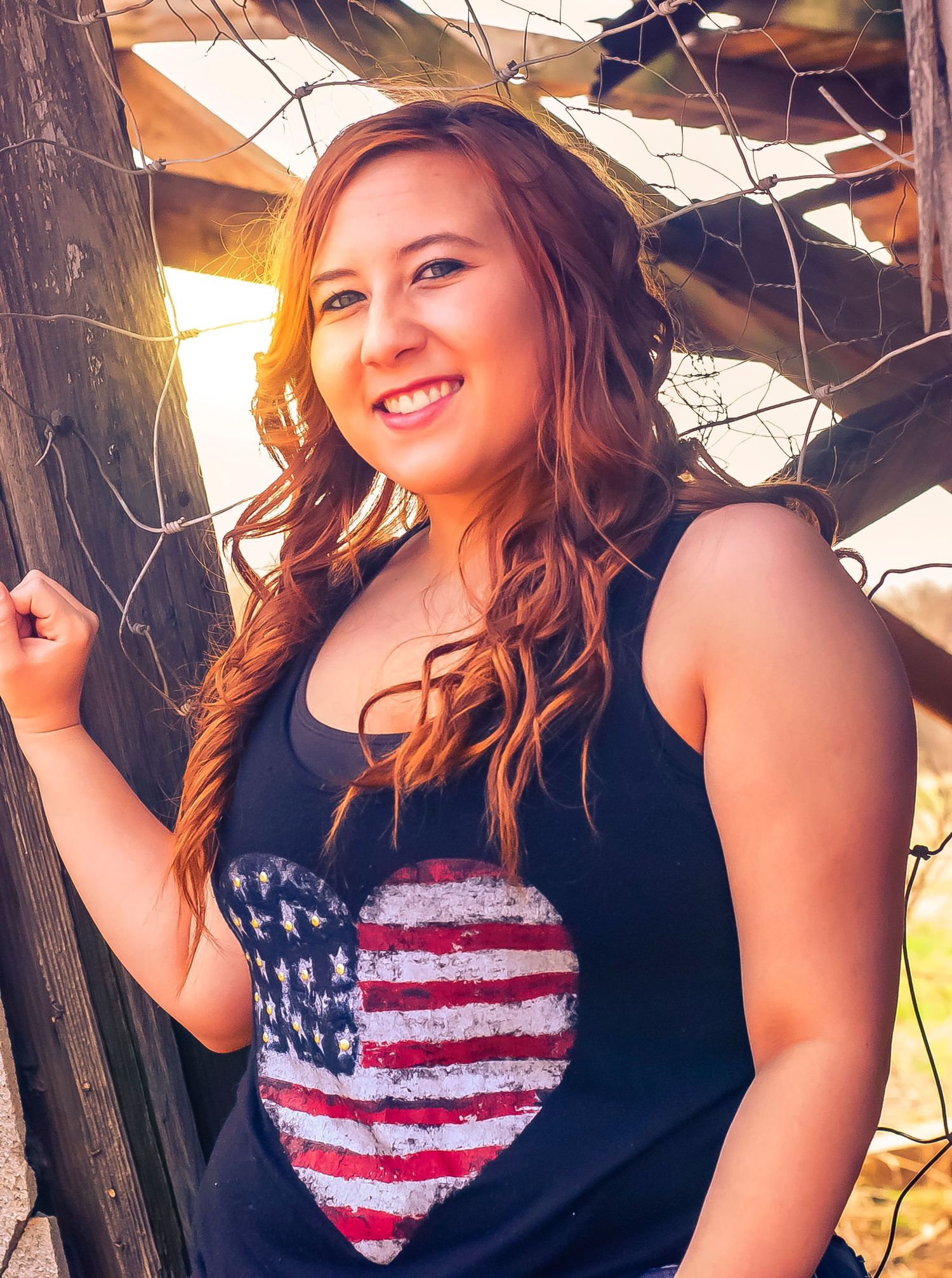 A young woman in a black tank top, featuring a heart design with the American flag, exudes beauty and patriotism.