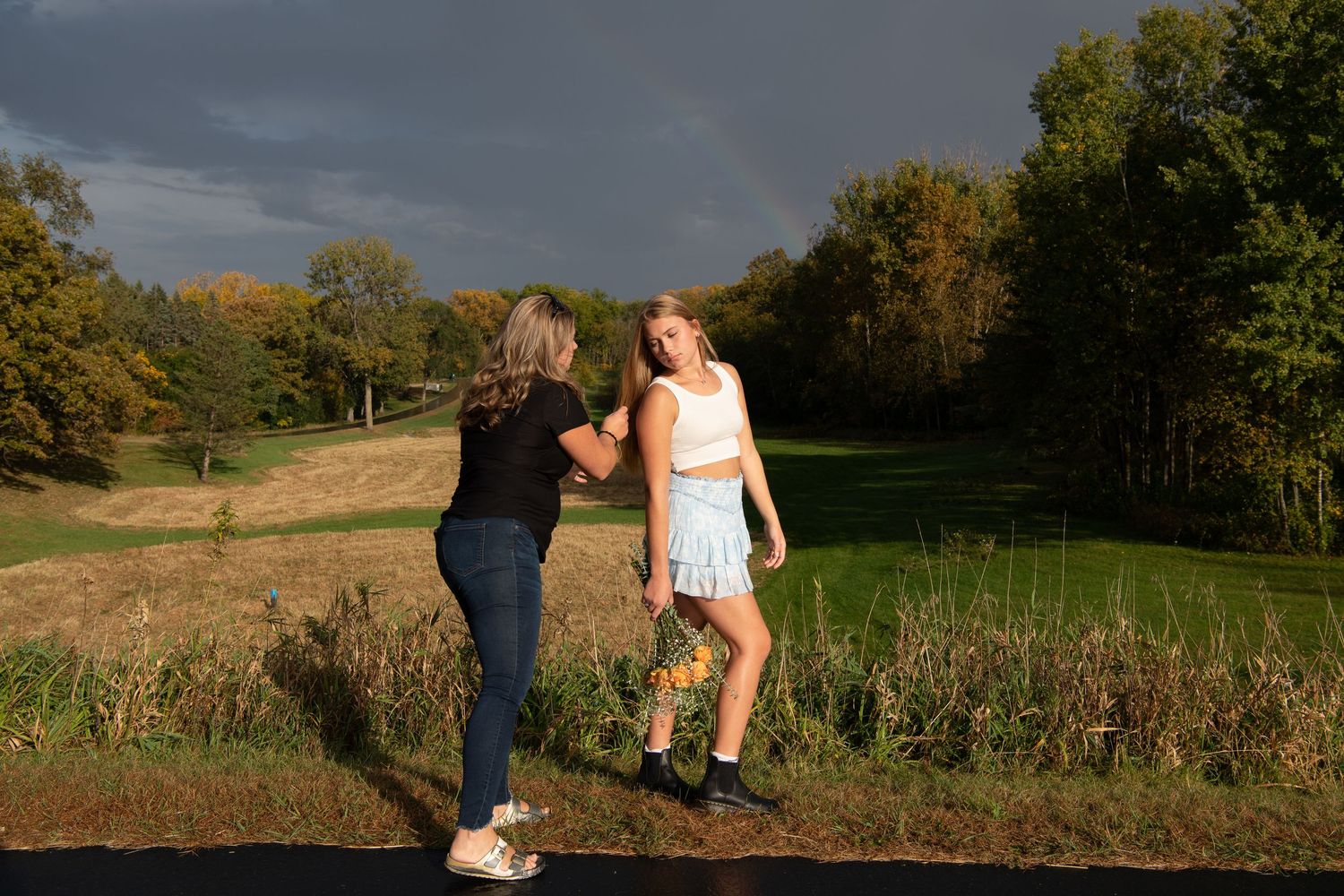 Two people walking together on a grassy rural path during golden hour with autumn trees in the background.