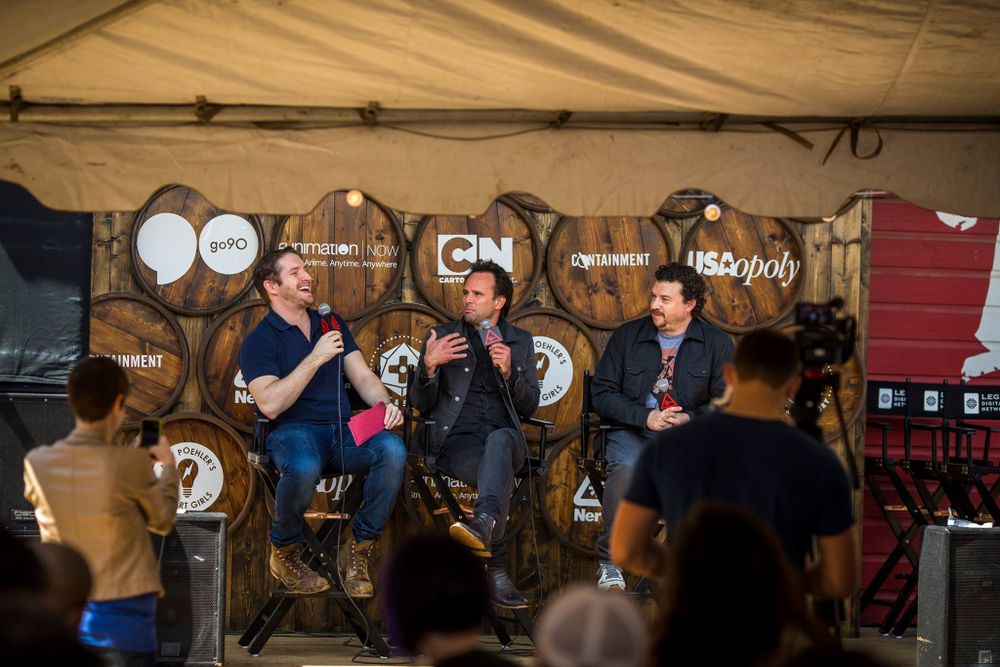 A panel discussion takes place inside a rustic barrel room with whiskey casks lining the wall behind the speakers.