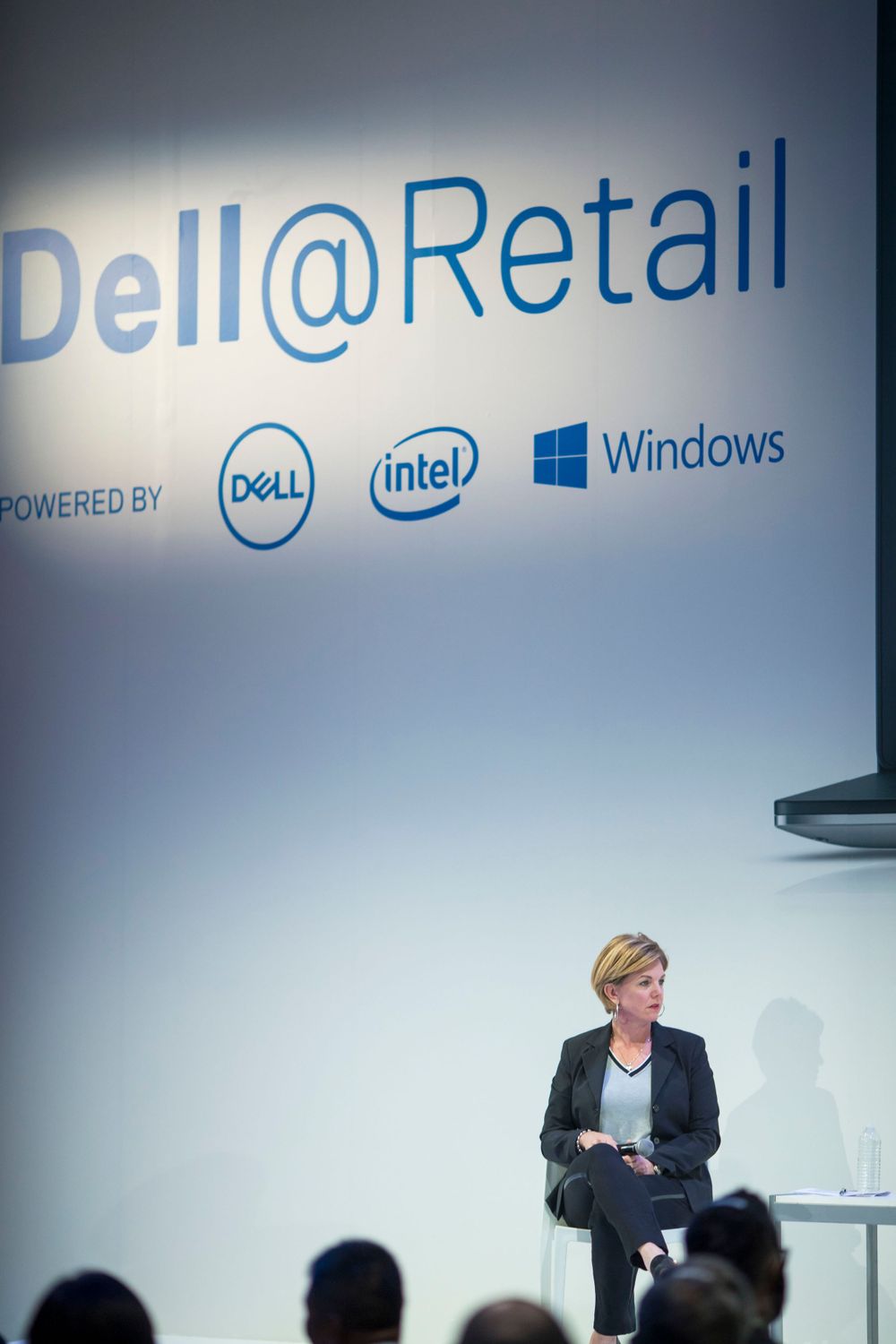 A speaker presents at a Dell Retail event with Dell, Intel and Windows logos displayed prominently on the backdrop.