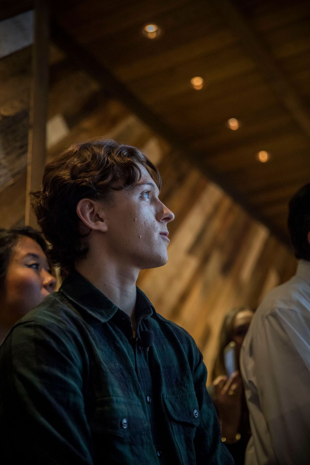 A person in a dark shirt gazes upward in a dimly lit indoor space with warm ceiling lights.