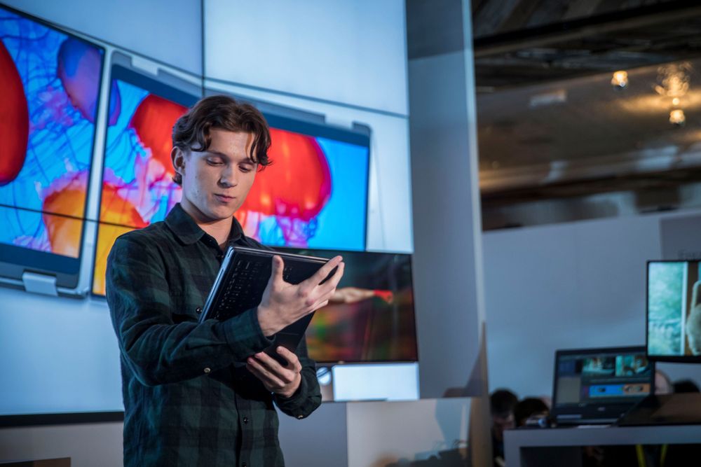 A person checks a notes on a digital tablet while standing in a modern office space with colorful digital displays on the wall.