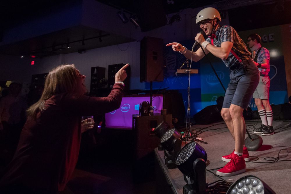 A performer in red shoes and shorts energetically singing on stage while engaging with audience members at a live show.