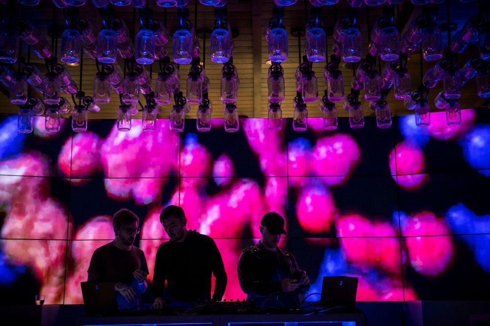 Silhouettes of people watching a dramatic pink and blue light show with illuminated hanging elements on stage.