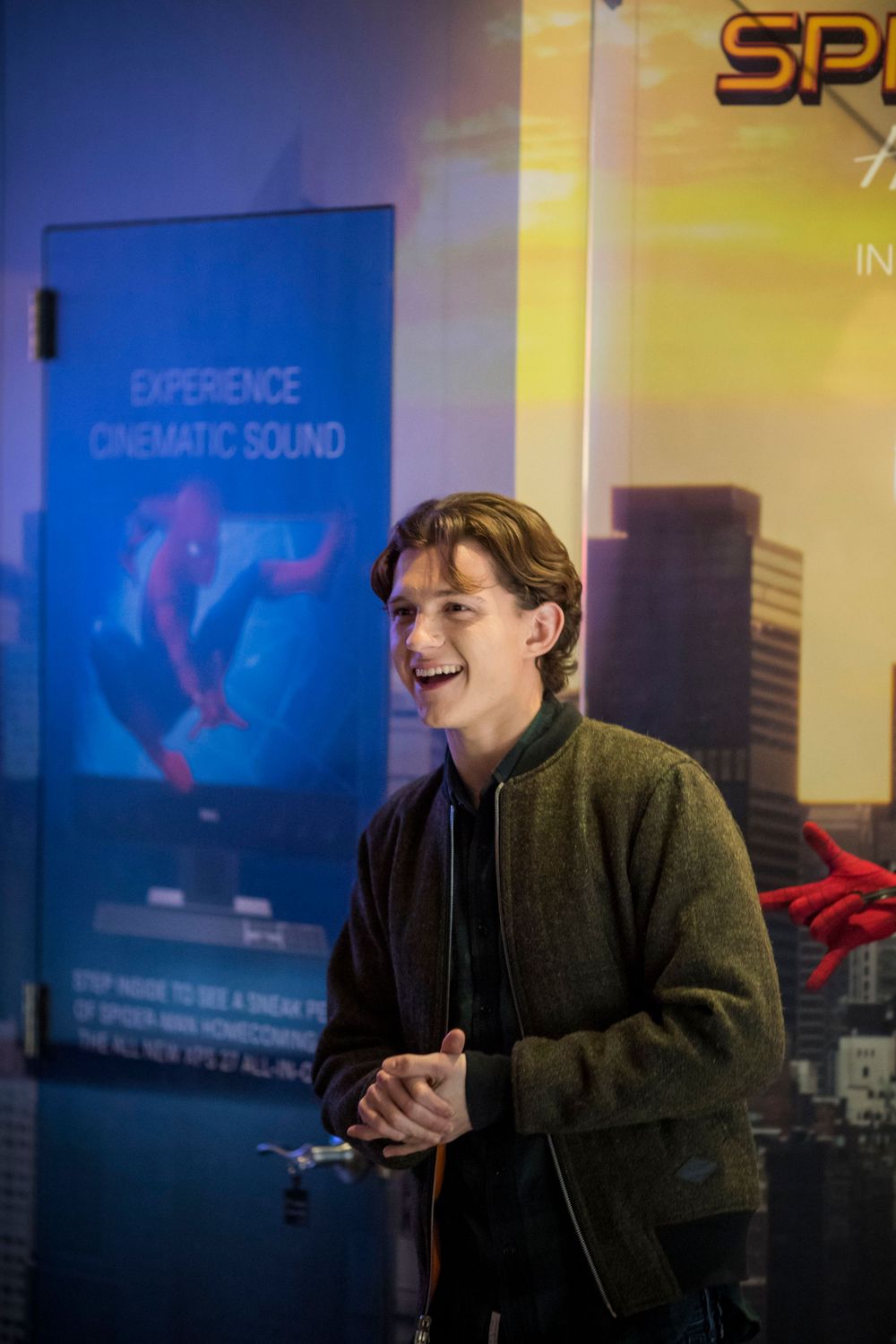 Someone laughs joyfully while standing in front of a blue cinematic sound experience display in a dimly lit setting.