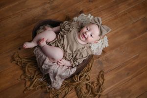 Baby lying on cozy textured blanket on hardwood floor laughing with pure joy during portrait session.