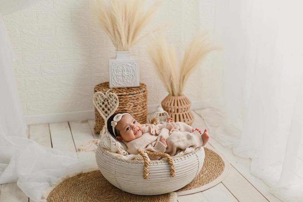 Cozy newborn photography setup with natural decor featuring woven basket, pampas grass and neutral tones on white wooden backdrop.