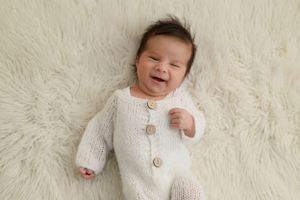 A happy baby lies on white fur wearing a cozy knit cardigan with wooden buttons.