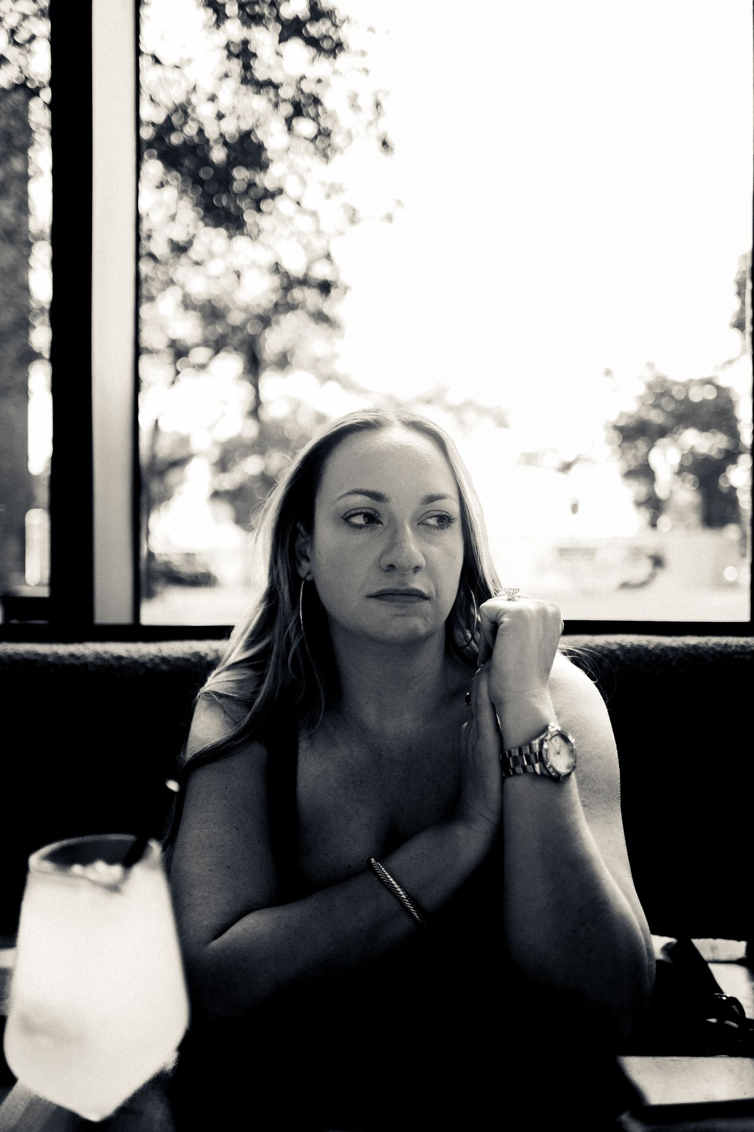 Black and white portrait of woman looking pensively out a window while seated on a couch.