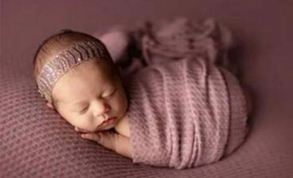 Sleeping newborn in soft pink wrap against dusky rose colored backdrop.
