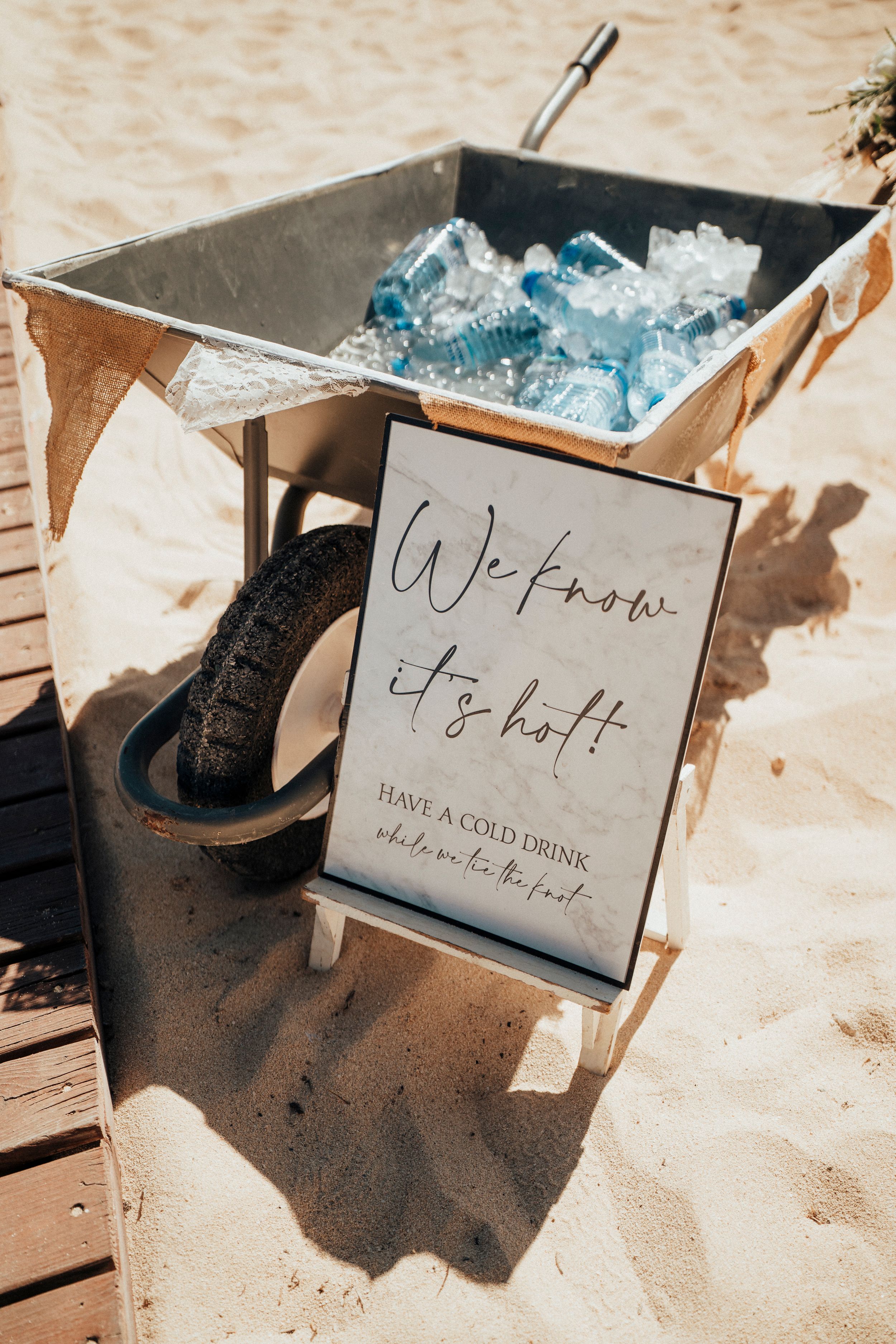 A wheelbarrow filled with ice cubes and a welcome sign on display at a rustic beach wedding setup.
