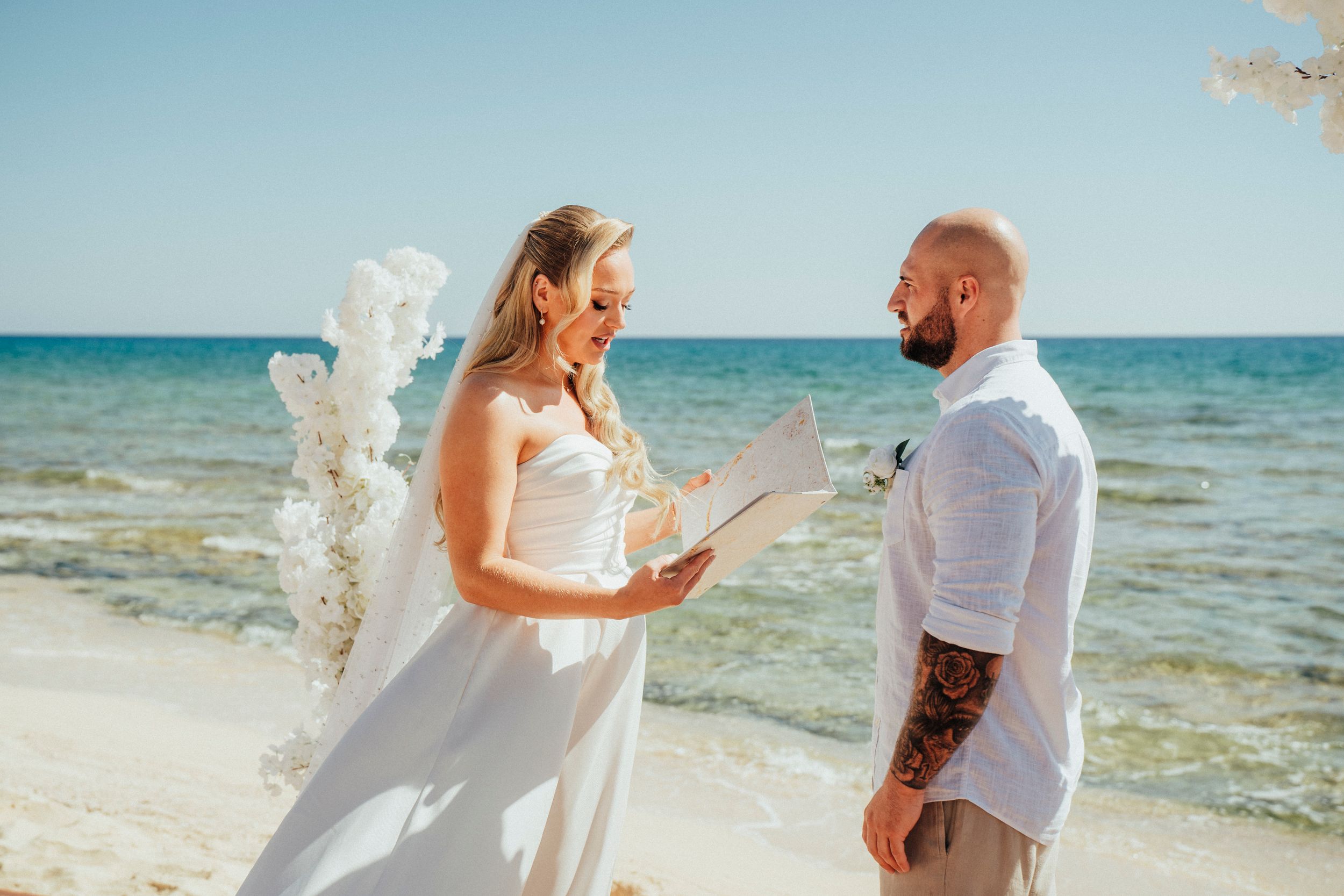 A wedding ceremony on a sunny beach with sparkling ocean waves and clear blue skies in the background.