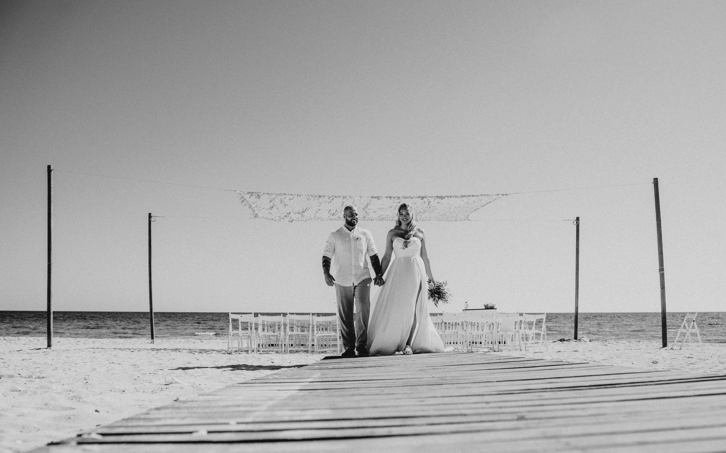A couple stands on a wooden walkway against a desert landscape backdrop during their outdoor ceremony.