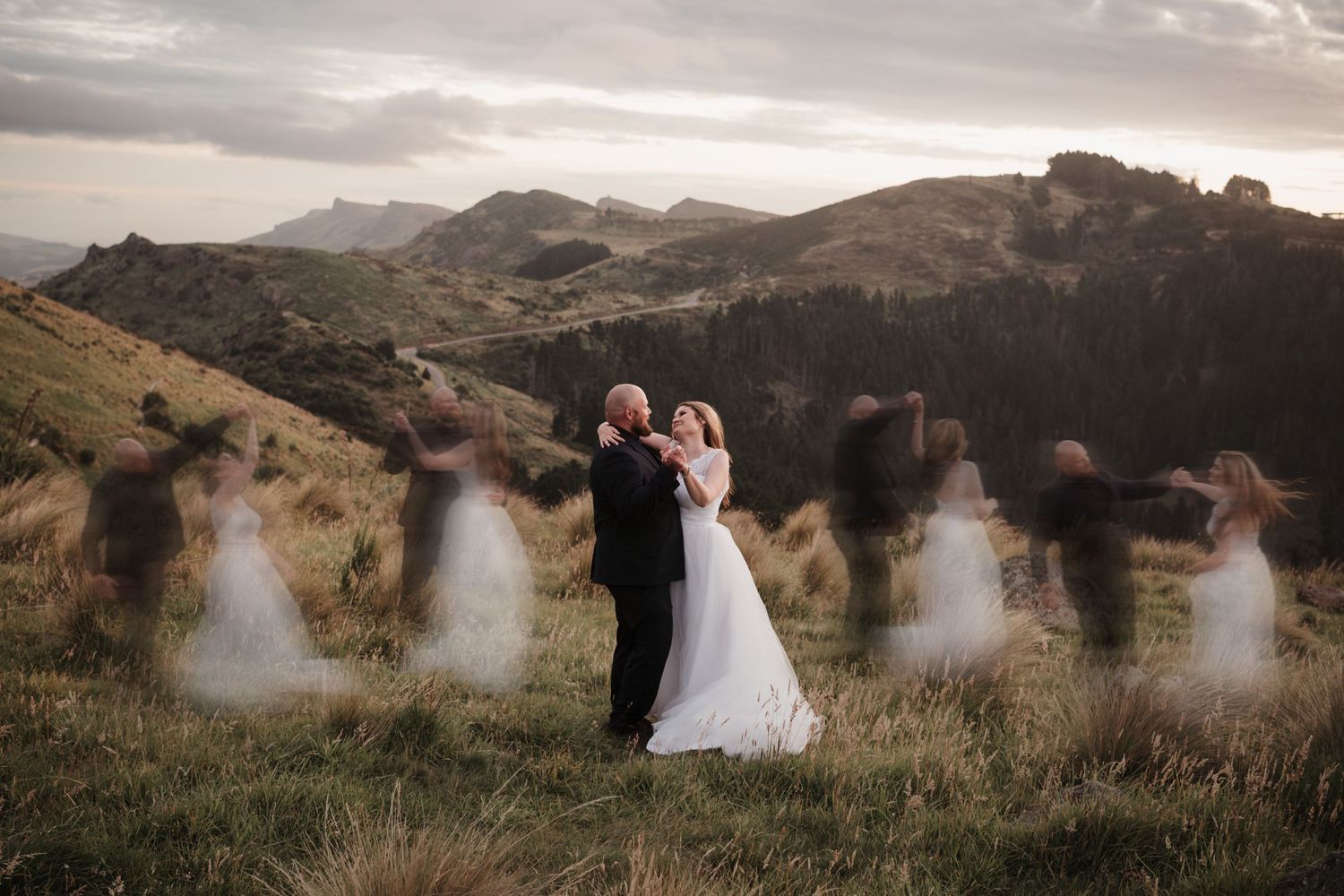 Ethereal wedding scene on a hilltop at sunset with blurred motion figures creating ghostly silhouettes in New Zealand landscape.
