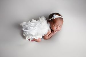 A sleeping newborn baby wrapped in soft white fabric against a light gray background.