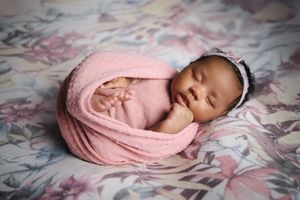 Sleeping newborn wrapped in soft pink swaddle blanket on floral bedding in professional photography session.