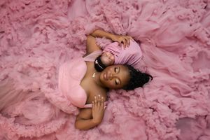 Person wearing a flowing pink tulle gown lies gracefully on a matching pink background Luxury Newborn baby photoshoot, Vanessa Charlotte