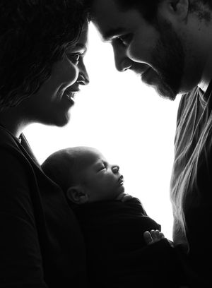 A silhouette portrait shows an intimate family moment with a newborn baby held between two adults in dramatic lighting.