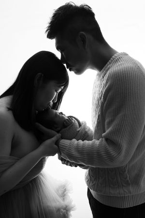 A tender black and white silhouette of two parents gazing down at their newborn baby with gentle affection.
